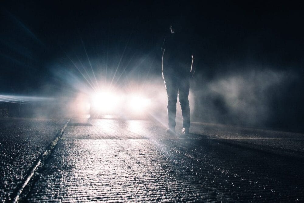 Mann steht im Scheinwerferlicht eines Fahrzeuges
