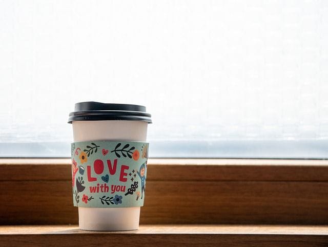To-Go Kaffeebecher steht auf einem Fensterbrett.