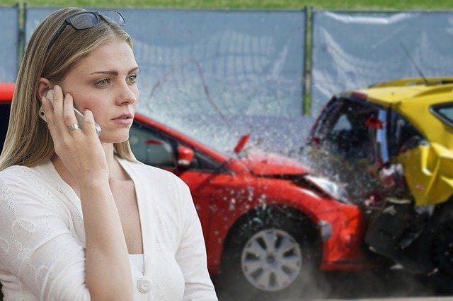 Frau steht vor einem Unfallwagen und telefoniert.
